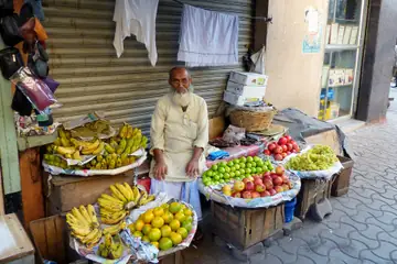 An elderly fruit seller sitting beside bananas, oranges, limes and apples laid out on the pavement
