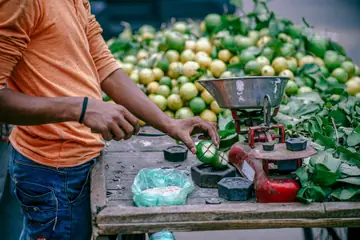 A seller's hand placing a weight on a scale beside a heap of green limes