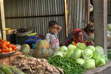 A woman selling cabbages, pumpkins, tomatoes, green chillies and ginger at her vegetable stall