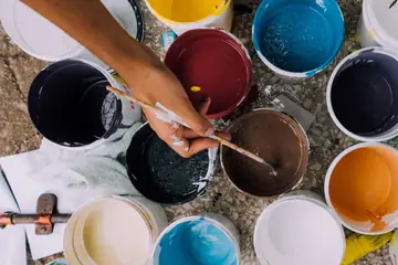 Open pots of paint in many colours and a hand dipping a brush