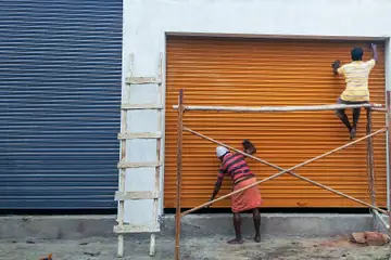 Two painters on a ladder and scaffold painting a shop shutter orange