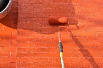 Painting work: a paint roller covering a brick wall in bright orange paint