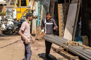 Two men moving a bundle of steel bars on a wooden cart in a street