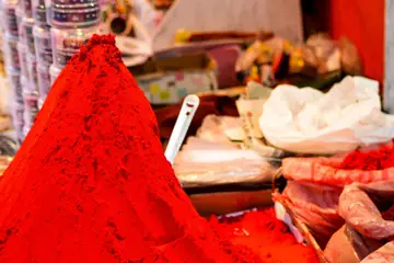 A heap of red chilli powder beside open sacks of spices