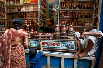 A woman and a child at a spice shop counter, with the shopkeeper reaching for jars on the shelves behind