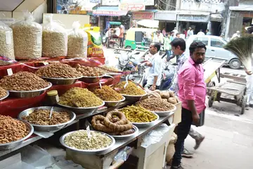 Steel bowls of almonds, dried fruit and nuts on a shop counter at Chandni Chowk, Delhi, with a shopper walking past