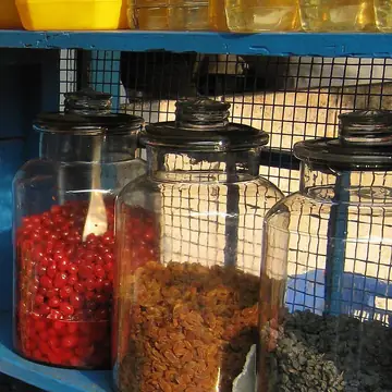 Large glass jars of red, brown and dark dried goods on blue shelves of a provision shop