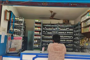 A customer at the counter of a small medicine shop with shelves of bottles behind