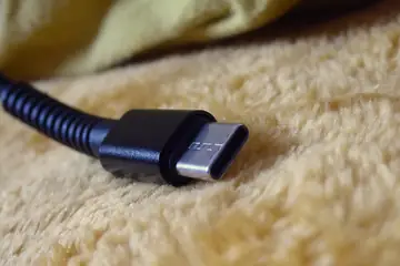 The USB-C plug of a black charging cable resting on a soft blanket