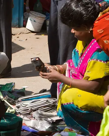A woman in a bright sari looking at a phone beside phone cases and cables at a street stall