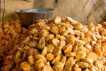 A heap of golden jaggery pieces with a steel bowl behind it