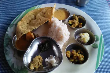 An Assamese thali with rice, papad and small steel bowls of curries on a plate at a roadside dhaba