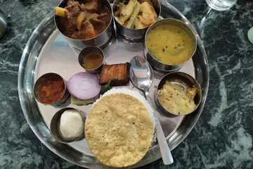 A Bengali thali on a steel plate with bowls of curry and dal, onion, papad and rice