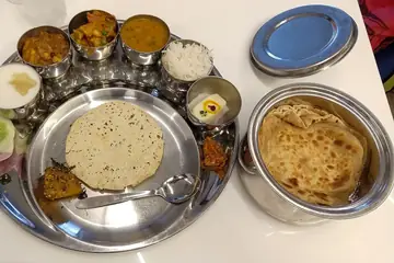 An Indore thali with bowls of vegetables, papad, rice and a paratha on a steel plate