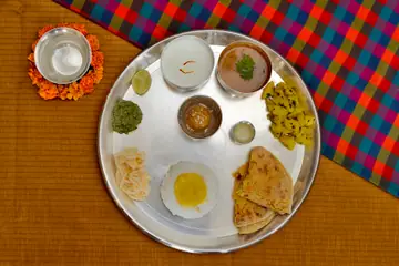 A Maharashtrian thali on a round steel plate with small bowls, chutneys, a paratha and a fried egg