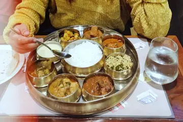 റസ്റ്റോറന്റ് മേശയിൽ കഴിക്കുന്നയാൾക്ക് വിളമ്പിയ, കറികളും ചോറും നിറഞ്ഞ ഒരുപാട് കിണ്ണങ്ങളുള്ള വൃത്താകൃതിയിലുള്ള പിച്ചള താലി