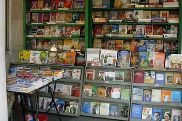 A roadside bookstall with green display shelves full of books and a table of books in front