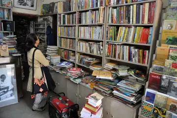 A woman browsing shelves and stacks of books inside a small bookshop