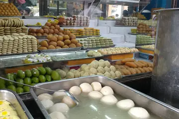 A sweet shop counter piled with trays of laddus, barfi and rasgullas in syrup
