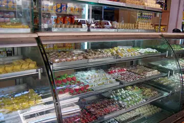 A curved glass counter with trays of mithai in many colours at a sweet shop in Goa