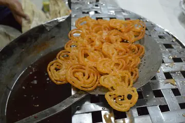 A heap of orange jalebis lifted out of the pan on a steel strainer
