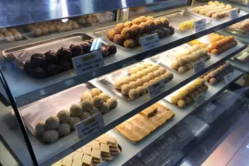 Trays of laddus and burfi with price cards in a sweet shop's glass counter in Chennai