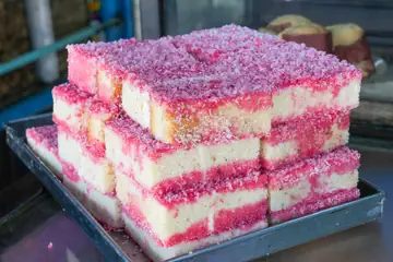 A stack of sponge cake squares topped with pink coconut on a bakery tray