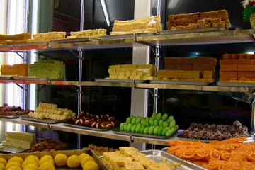 Steel shelves stacked with trays of barfi, laddus, pistachio sweets and jalebi