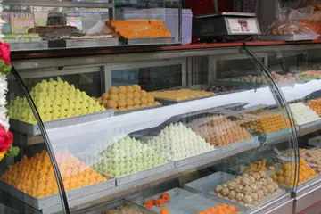 A glass counter of modaks, laddus and burfi with a weighing scale on top