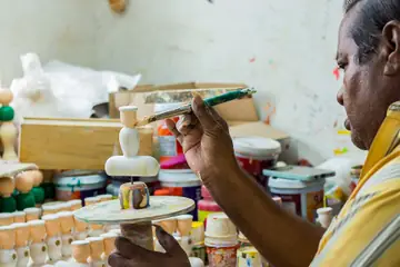 নিজৰ কাৰখানাত সৰু ঘূৰণীয়া পাটাত কাঠৰ খেলনা ৰং কৰি থকা খেলনা বনোৱা মানুহ