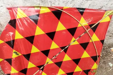 A red and yellow diamond-patterned paper kite with a cane spine